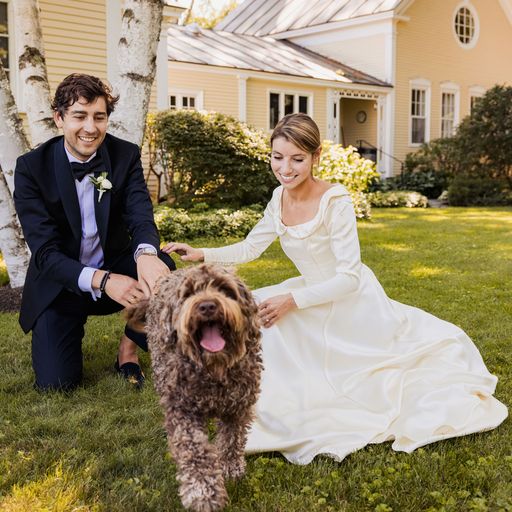 Bride and groom smiling at their labradoodle dog on wedding day