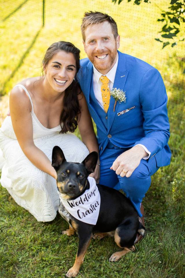 Bride and groom posing with their dog who is wearing a bandana that says Wedding Crasher