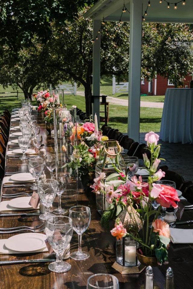 Dinner table set for outdoor wedding with bright pink flowers down the center