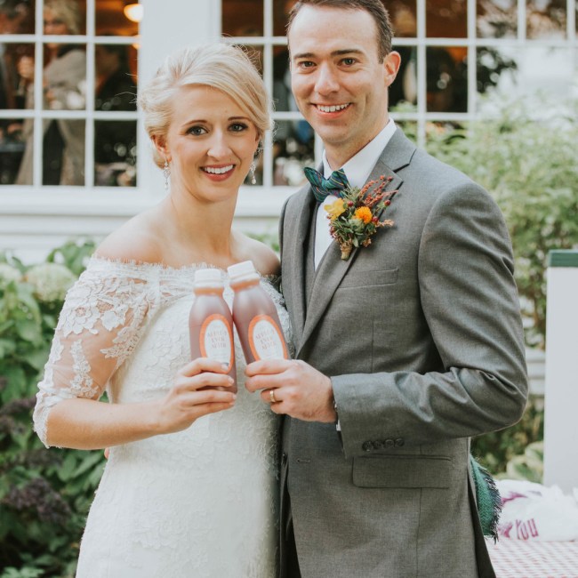 Bride and groom holding custom apple cider favors at Vermont fall wedding