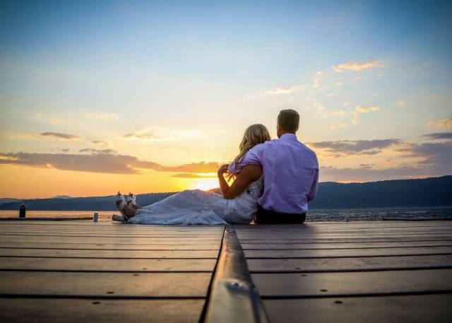 Bride and groom sitting on dock looking over the sunset during Vermont wedding