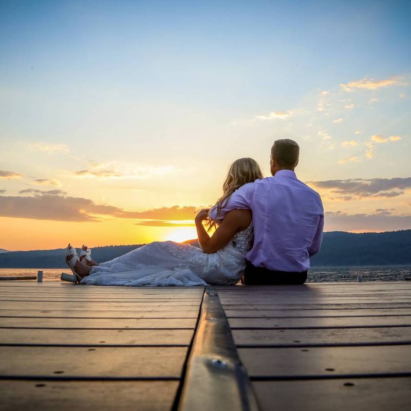 Bride and groom sitting on dock looking over the sunset during Vermont wedding
