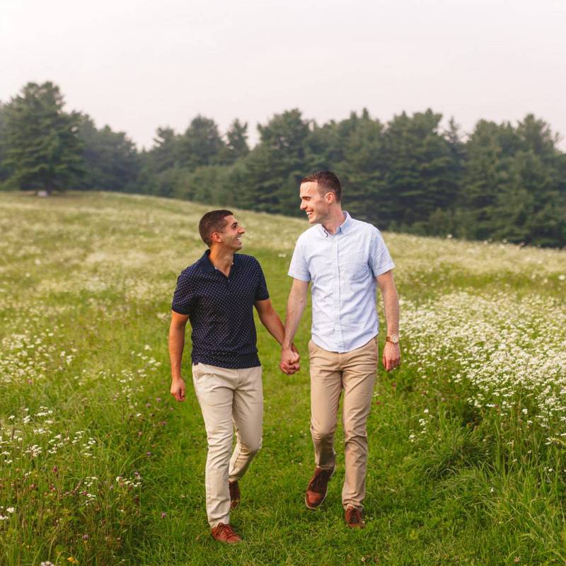 Grooms walking in field in Vermont during engagement photoshoot
