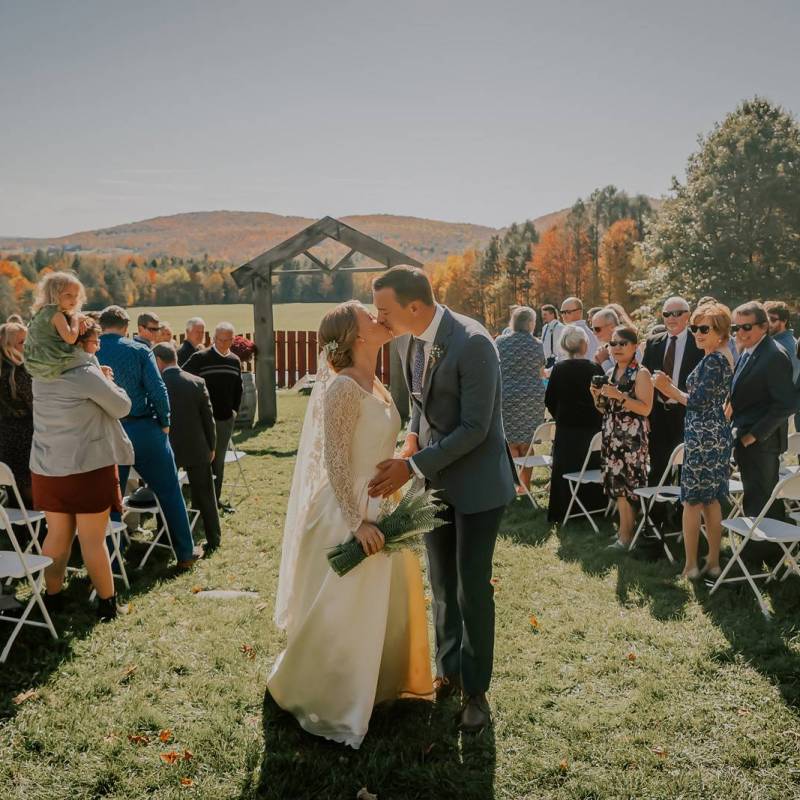 Bride and groom kissing at the end of their outdoor ceremony aisle during Vermont wedding at the Inn at Grace Farm