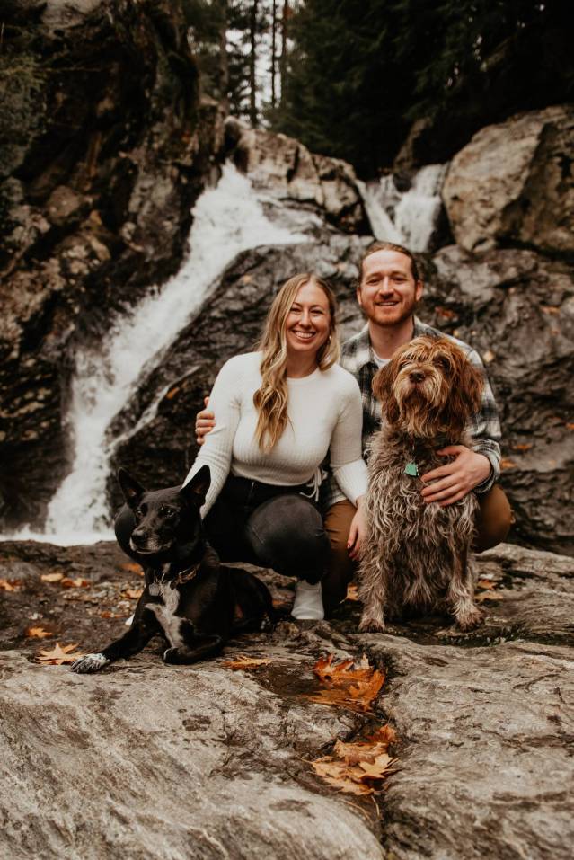 hiking couples with dogs at a waterfall for engagement photos