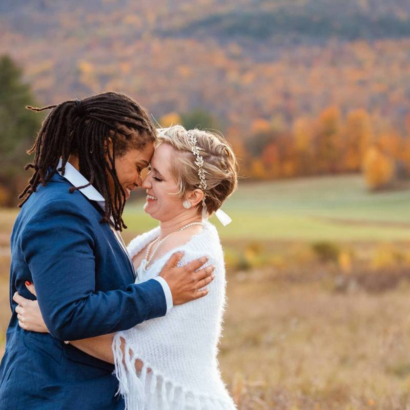 Black bride and white bride nuzzling in front of bright foliage during Vermont fall wedding