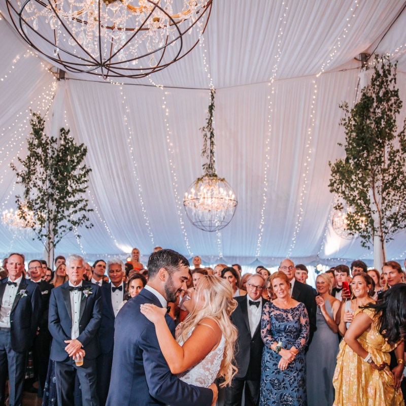 White bride and groom dancing under a tent draped with chandeliers on wedding day in Vermont