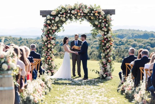 Bride and groom exchanging vows under floral ceremony archway