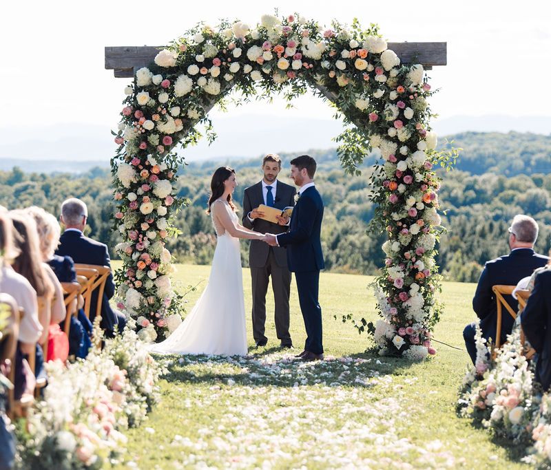 Bride and groom exchanging vows under floral ceremony archway