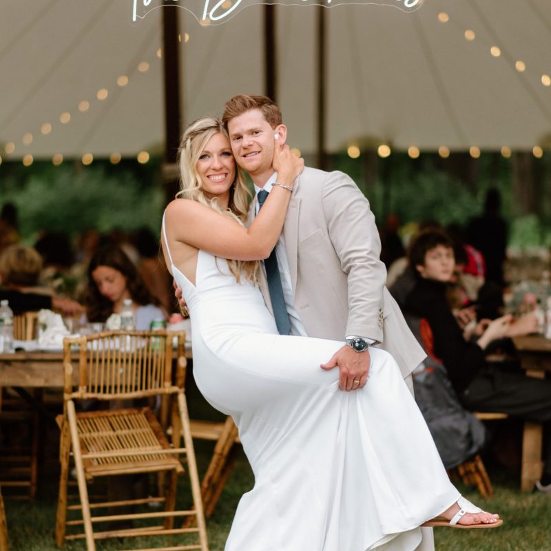 bride and groom standing in front of neon sign with their last name