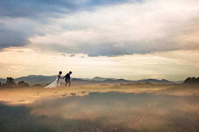 Bride and groom walking up a hill at sunset with dramatic clouds and mist