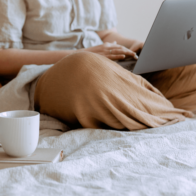 stock image of woman sitting on bed with laptop and coffee